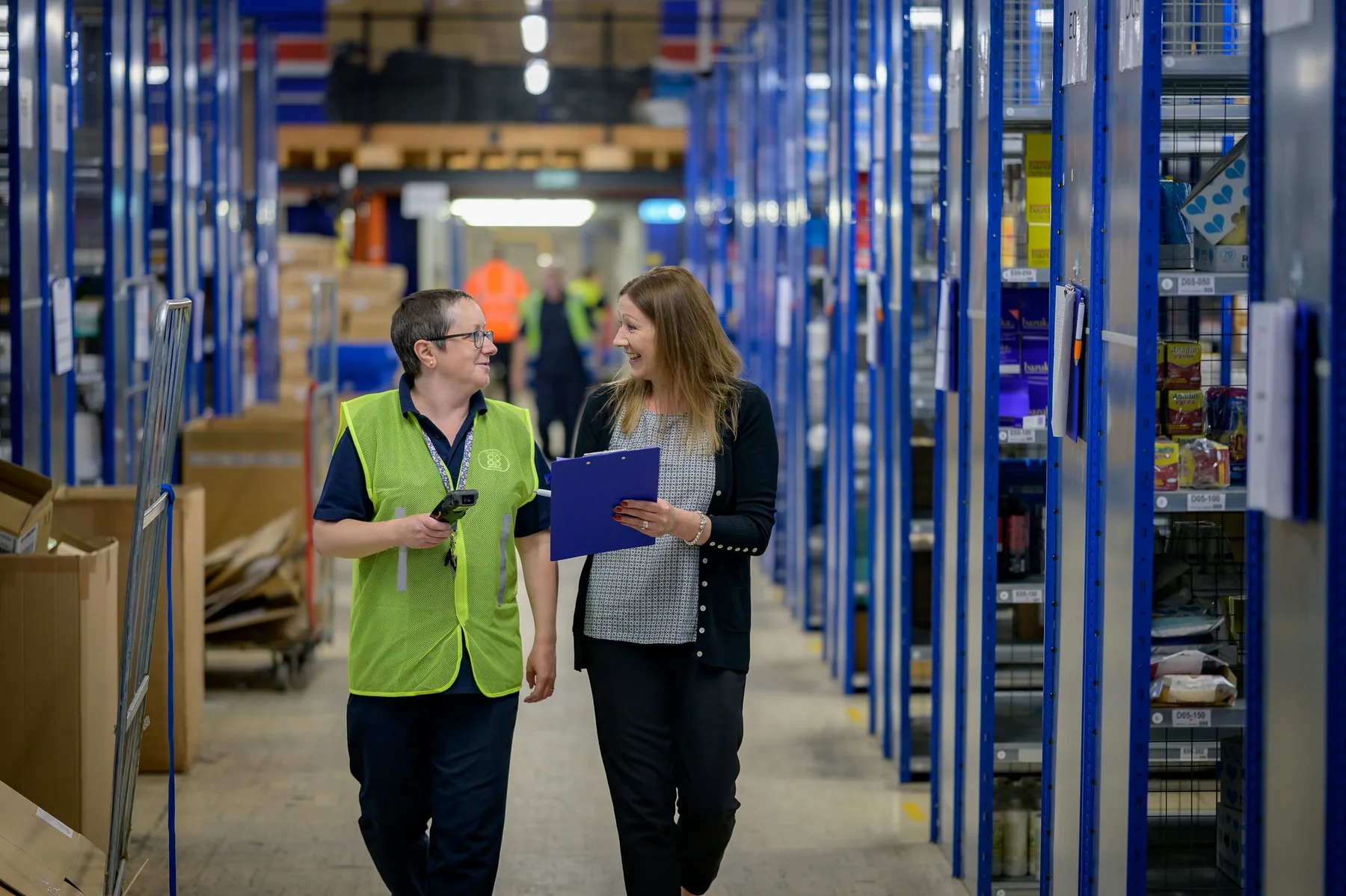Two people discuss a document in a warehouse aisle. Illustrative stock photography, not a Harborline client engagement.
